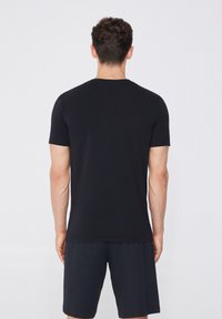 Černé tričko s krátkým rukávem z hladkého, lehkého materiálu, s jednoduchým, klasickým střihem a kulatým výstřihem. Nosí se s tmavými šortkami.