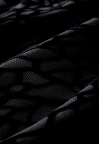 Sort tekstureret stof med et geometrisk mønster, der har en blanding af glatte og forhøjede overflader. Designet giver visuel dybde og kontrast.