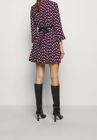 Krótka sukienka w geometryczny wzór w kolorach granatowym, białym i różowym, z wiązaniem w talii i długimi rękawami. Połączona z czarnymi kozakami do kolan.