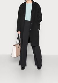 Schwarzer Wollmantel mit lockerer Passform, einreihigem Design, kombiniert mit einem hellblauen Pullover und schwarzen Hosen. Hellrosa und weiße Tote-Tasche.