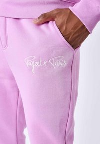 Zachte lichtroze sweatpants met een elastische tailleband, zijzakken en witte geborduurde tekst "Project x Paris" op de zak.
