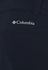 Marineblå skjorta i tyg med en slät struktur, med en vit Columbia-logotyp som tydligt syns på bröstet.