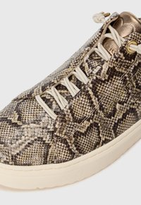 Baskets texturées avec un motif en imprimé serpent brun et beige, des lacets crème et un accent doré près des œillets. Semelle en caoutchouc.