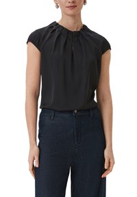 Blouse noire à manches courtes avec un col plissé et un détail en forme de clé. Fabriquée en tissu lisse, associée à un pantalon en denim sombre taille haute.