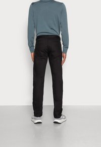 Pantalones negros combinados con un suéter azul claro, con un corte recto y bolsillos traseros visibles. Los pantalones tienen una textura suave.
