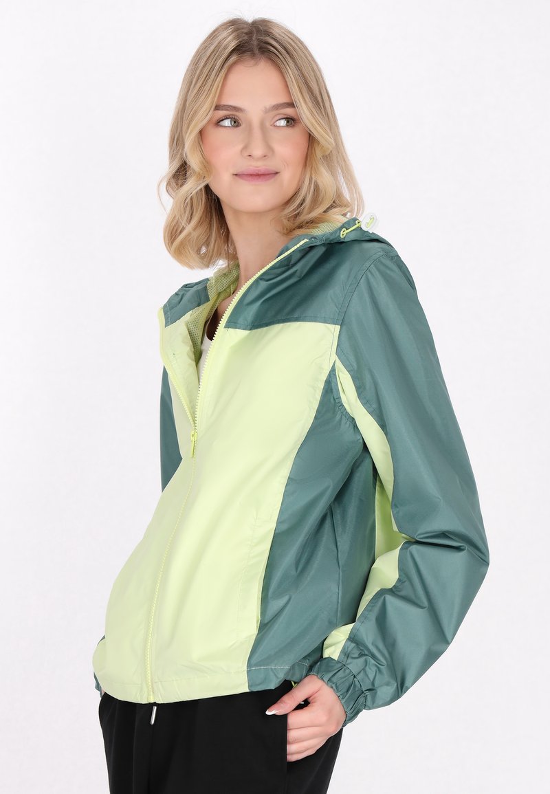 Chaqueta tipo rompevientos con un cuerpo verde claro y acentos en verde oscuro, cierre frontal de cremallera completa, capucha ajustable y puños elásticos.