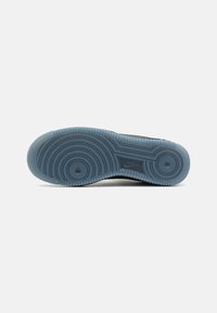 Zapatilla deportiva negra con una suela de goma azul transparente que presenta patrones de tracción circulares y ondulados. Incluye un logo visible grabado en la suela.