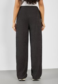 Pantalons larges à rayures texturées et foncées avec une taille haute, présentant une coupe ample et des variations subtiles dans le motif du tissu.