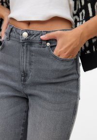 Visoke sivo kavbojke iz denimske tkanine z gladko teksturo, z zapiranjem na srebrn gumb in stranskimi žepe.