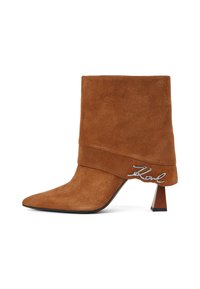 Stivale alla caviglia in suede marrone con punta affilata, tacco a blocco angolato e un design decorativo piegato che presenta un accent metallico a forma di "K".