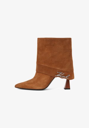 Rudi zomšiniai auliniai batai su smailiu pirštu, įstrižiniu tradiciniu kulnu ir dekoratyvine sulenkta dizaino detalė, kurią puošia metallic "K" akcentas.