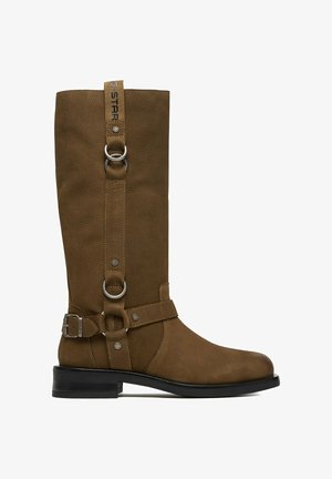 Brązowy skórzany kozak za kolano z srebrnymi klamrami, pierścieniami i czarną podeszwą, z pionowymi paskami i markową pętelką u góry.