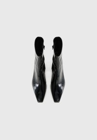 Bottines noires à finition brillante, avec des pointes en forme de flèche et une fermeture éclair sur le devant. Le design présente un matériau texturé semblable au cuir.