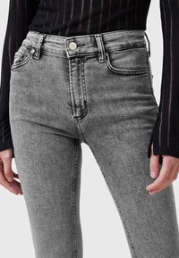 Jeans in denim grigio a vita alta con una texture liscia. Presentano un bottone frontale, cinque tasche e un design classico a cinque tasche.
