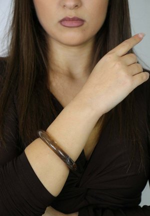 Bruine doorschijnende armband gemaakt van hars, cirkelvormig ontwerp met een gladde textuur, gedragen om de pols, in contrast met de huidskleur.