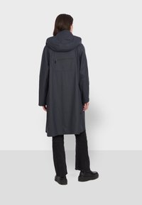 Długi granatowy płaszcz z kapturem, wykonany z gładkiego, wodoodpornego materiału. Posiada zapinaną na zamek tylną kieszeń oraz elegancki, minimalistyczny design.