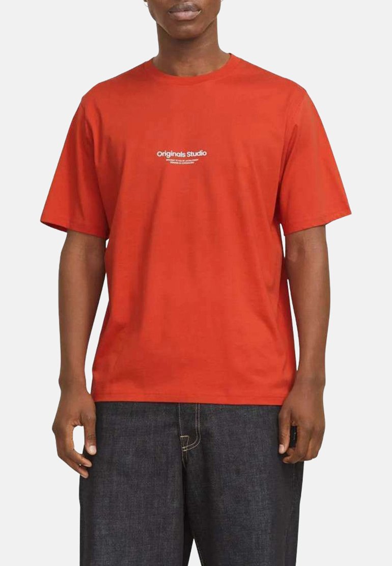 Rød bomulds T-shirt med rund halsudskæring, korte ærmer, med et hvidt logo trykt på brystet. Båret med mørkeblå denim bukser.