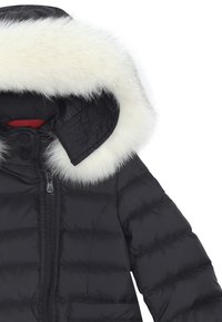 Giacca a puffo nera con texture trapuntata, dotata di un cappuccio con bordo in pelliccia sintetica bianca, chiusura con zipper e rivestimento rosso al colletto.