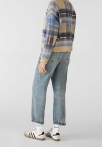 Pull en mélange de laine à carreaux beige et bleu, assorti à un jean bleu délavé et des baskets blanches. L'ensemble présente une coupe décontractée avec des accents côtelés.