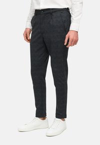 Grijs geruite broek met een getailleerde pasvorm, voorzien van een platte voorkant, zijzakken en een subtiele textuur. Draagt witte sneakers.