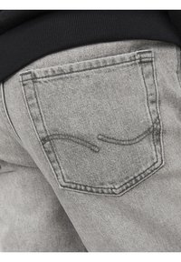 Grå denimjeans med stickade bakfickor, med en slät yta och subtil blekning. Svart midjeband ovanför jeansen.