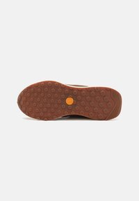 Brown rubber shoe sole with hexagonal grip patterns and a central logo. Slightly raised edges and textured finish for durability.
