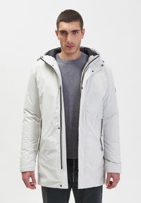Męski biały ocieplany parka z kapturem, zapinany z przodu na zamek, z bocznymi kieszeniami i ciemnym swetrem pod spodem. Gładka tekstura, nowoczesny design.