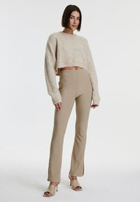 Beige cropped trui met een textuur gebreid, gecombineerd met beige uitlopende broeken met zijsleuven, en tan open teen hakken.
