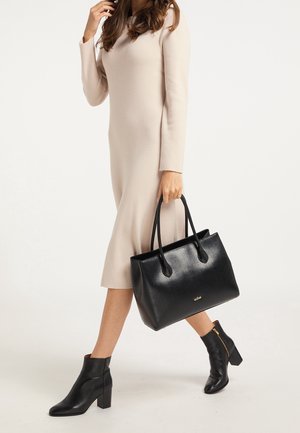 Femme en robe midi beige à manches longues marchant, tenant un sac à main en cuir noir et portant des bottines noires à talons blocs.
