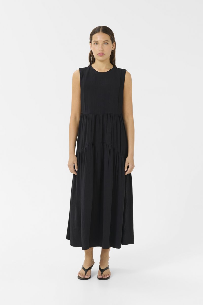 Vestido maxi preto sem mangas, com decote redondo, design em camadas e um ajuste solto. Tecido suave e texturizado, sem padrões ou detalhes visíveis.