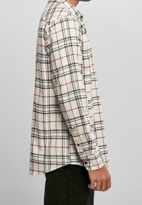 Lange mouwen geruite shirt in crèmekleur, zwart en rood. Voorzien van knoopmanchetten, een rechte pasvorm en een zijsplit aan de onderkant. Gemaakt van katoen.