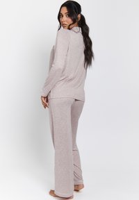 Conjunto de loungewear de manga larga en un suave color rosa claro, con textura acanalada y ribete blanco en contraste; incluye una parte superior y pantalones de pierna ancha a juego.