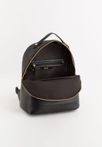 Mochila negra texturizada con cremallera dorada, cuenta con un bolsillo interior con cremallera y un compartimento grande, además de un asa resistente en la parte superior.