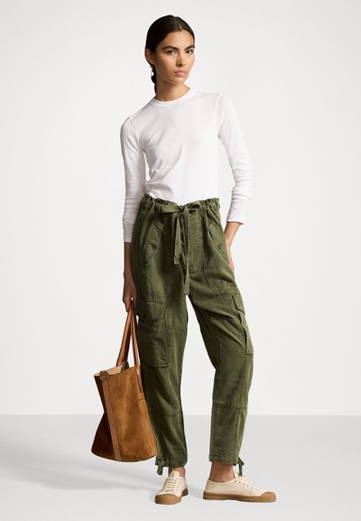 Groene katoenen cargo broek met meerdere zakken, witte lange mouwen shirt, beige sneakers en een bruine suède schoudertas. Glad stoftextuur.