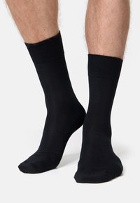 Schwarze Crew-Socken aus glattem Stoff, mit einem gerippten Bündchen für zusätzlichen Komfort. Standardform ohne sichtbare Muster oder Akzente.