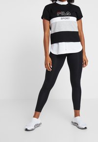 Sportovní top s černými a šedými bloky, bílá pod tričkem, černé legíny a bílé boty s leopardím potiskem.