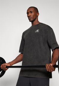 Dunkelgraues, übergroßes T-Shirt aus weichem Baumwollstoff, mit einem kleinen weißen Champion-Logo auf der Brust. Der Stoff hat eine gewaschene Textur.