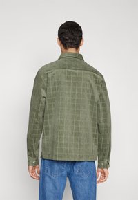 Groene ribfluwelen jas met verticale strepen, knopenmanchetten en een standaard kraag. Beschikt over een gestructureerde oppervlakte en een ontspannen pasvorm.