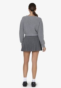 Grijze geribde trui met een cropped ontwerp, gecombineerd met een grijze plooienrok. Bevat plooien en een aansluitende tailleband voor structuur.