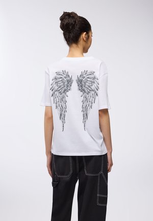 T-shirt bianco a maniche corte con un dettagliato design di ali nere stampato sul retro. Abbinato a pantaloni neri a gamba larga.