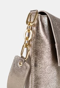 Borsa a mano metallica argento con superficie testurizzata, dettagli in oro, tra cui una tracolla a catena e un piccolo tag attaccato.