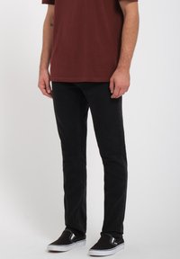 Men's black jeans with a slim fit, made of cotton blend fabric, featuring a classic five-pocket design and visible stitching details.