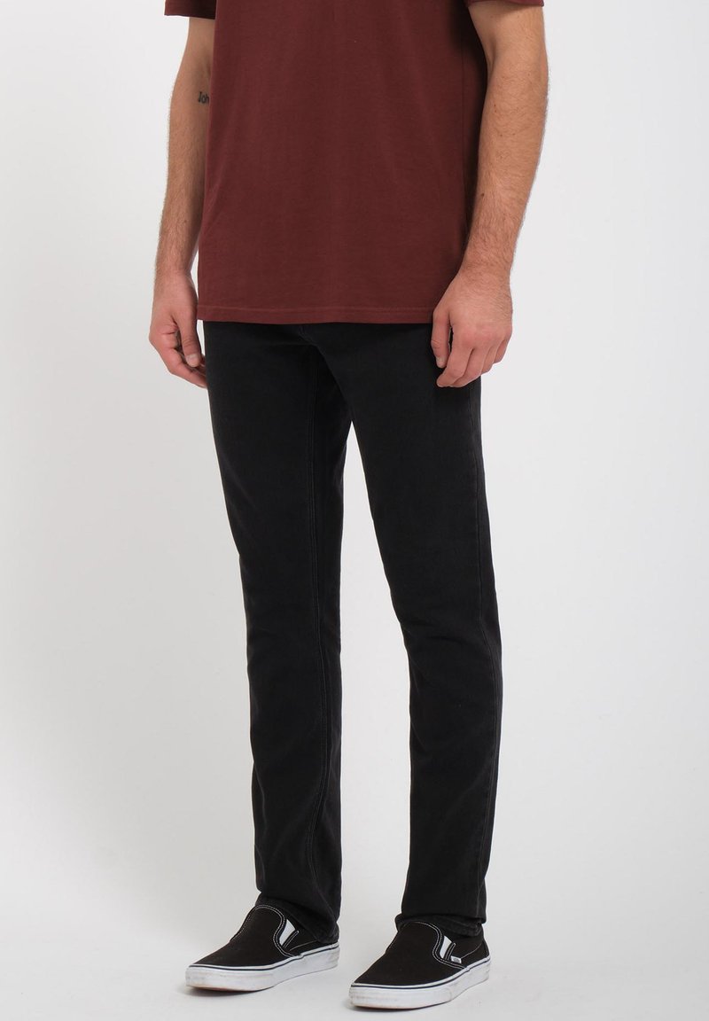 Men's black jeans with a slim fit, made of cotton blend fabric, featuring a classic five-pocket design and visible stitching details.