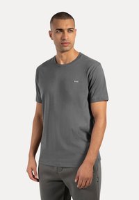 Graues Baumwoll-T-Shirt mit Rundhalsausschnitt, kurzen Ärmeln und einem kleinen Logo-Patch auf der Brust. Weicher Stoff und normale Passform.