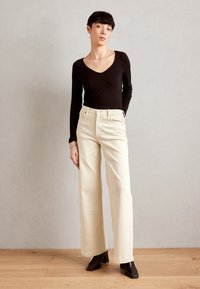 Light beige wide-leg jeans with a high waist, five-pocket design, and subtle stitching, paired with a fitted black long-sleeve top.