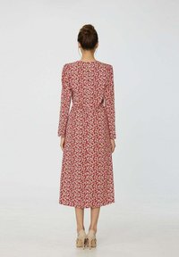 Robe florale rouge avec des manches longues, corsage ajusté et jupe midi fluide. Présente une ouverture en forme de clé au dos et un tissu doux et léger.