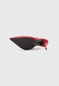 Zapato de tacón alto de charol rojo con puntera puntiaguda y tacón de aguja. La suela es negra, con una superficie lisa y una ligera curvatura.