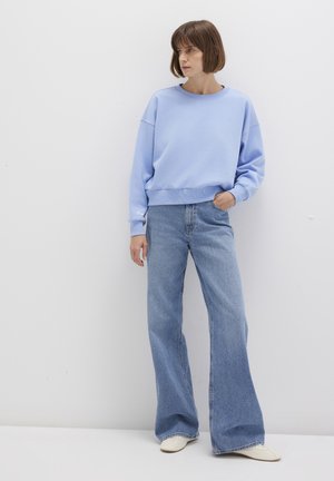 Helles blaues Sweatshirt mit rundem Halsausschnitt und überschnittenen Schultern, kombiniert mit hoch taillierten, weiten blauen Jeans und weißem Schuhwerk.