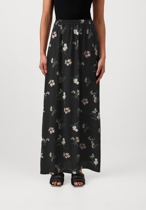 Jupe noire longueur cheville avec petit motif floral rose et blanc, portée avec un top noir sans manches et des sandales noires ouvertes à l’avant.
