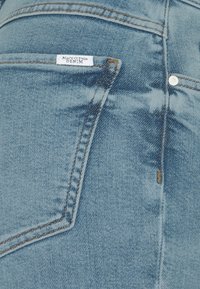 Světle modré džíny z denimu s klasickým designem, viditelným šitím, malou značkovou etiketou a kapsou s zakřiveným okrajem.